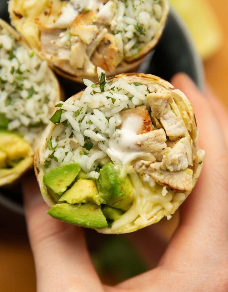 Chicken Avocado Burrito overhead shot of hand grabbing on to sliced open burrito