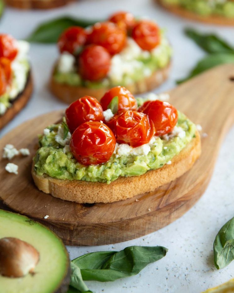 tomato avocado toast on wooden board surrounded by toast and garnish