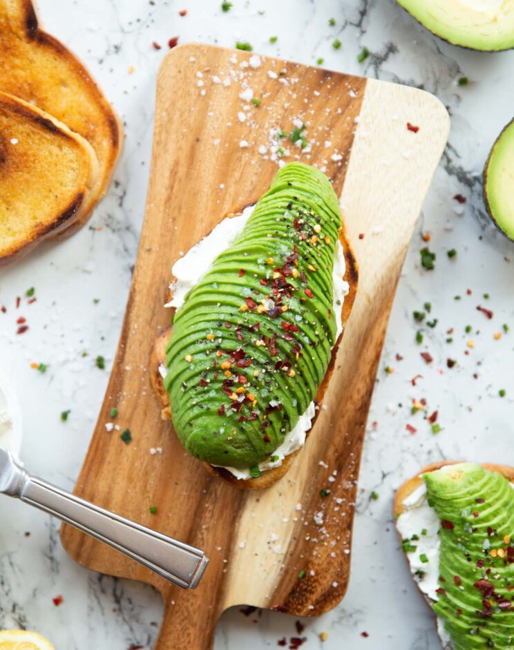 avocado cream cheese toast overhead shot of cream cheese avocado toast on chopping board surrounded by garnish