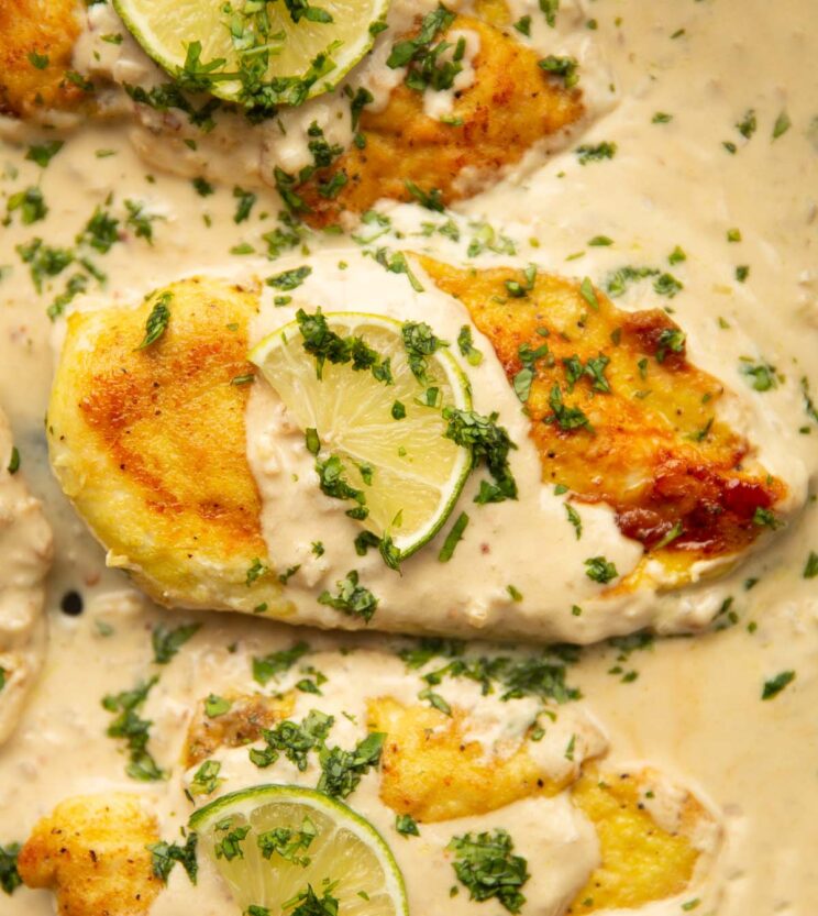 creamy coconut lime chicken breasts overhead close up shot of 3 creamy coconut lime chicken breasts in pan garnished with lime and coriander