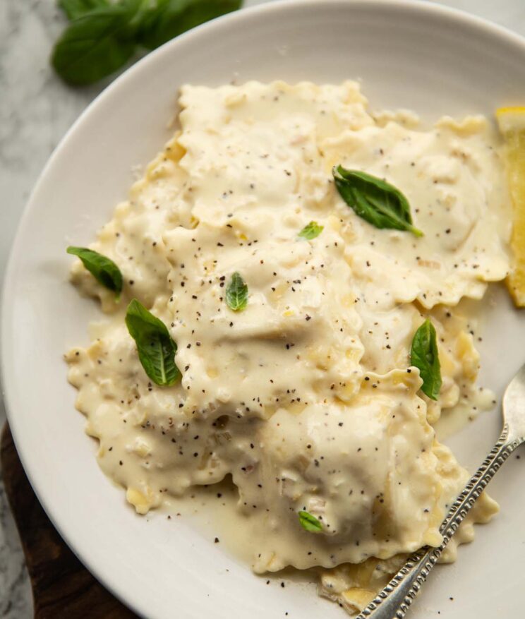 overhead shot of creamy lemon ravioli on small white plate with fresh basil