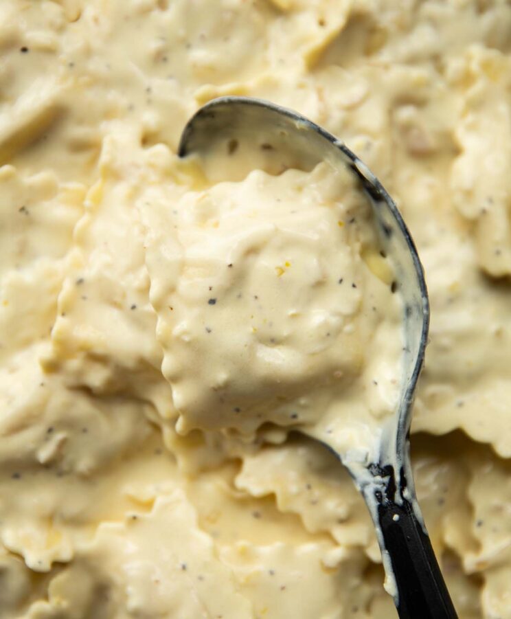 close up shot of black serving spoon digging into pan of lemon cream ravioli