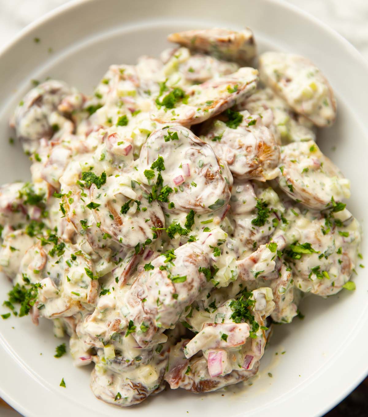 smashed potato salad in large white bowl garnished with parsley