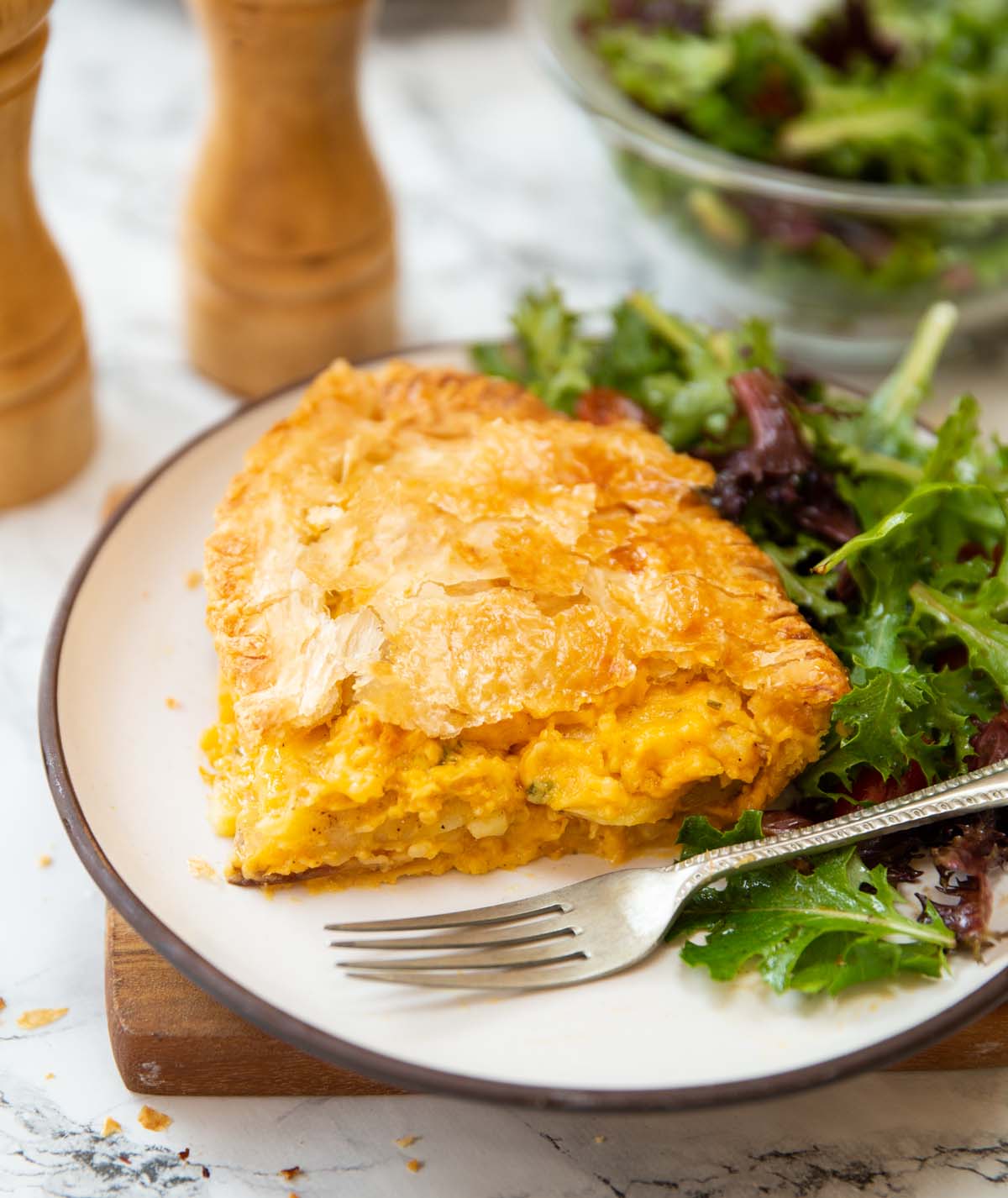 slice of potato cheese onion pie on small white plate with side salad and silver fork