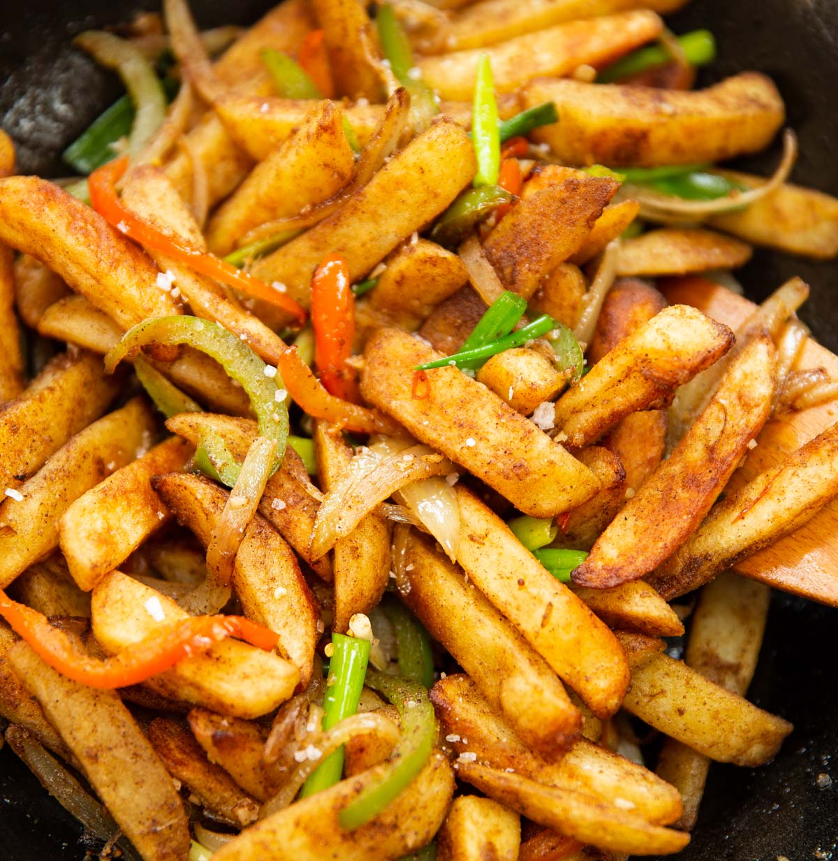 close up shot of salt and chilli chips in wok with wooden spoon