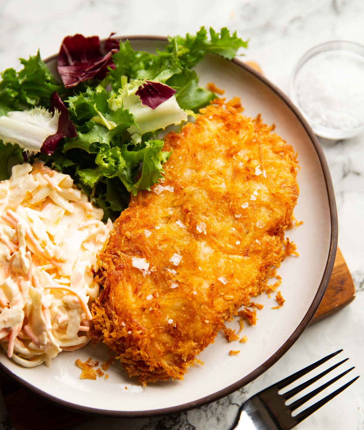 hash brown chicken served on small white plate with salad and coleslaw